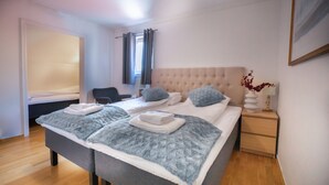 Una cama bien hecha con un colcha gris, una mesita de noche con un florero y una silla en una habitación de hotel.
