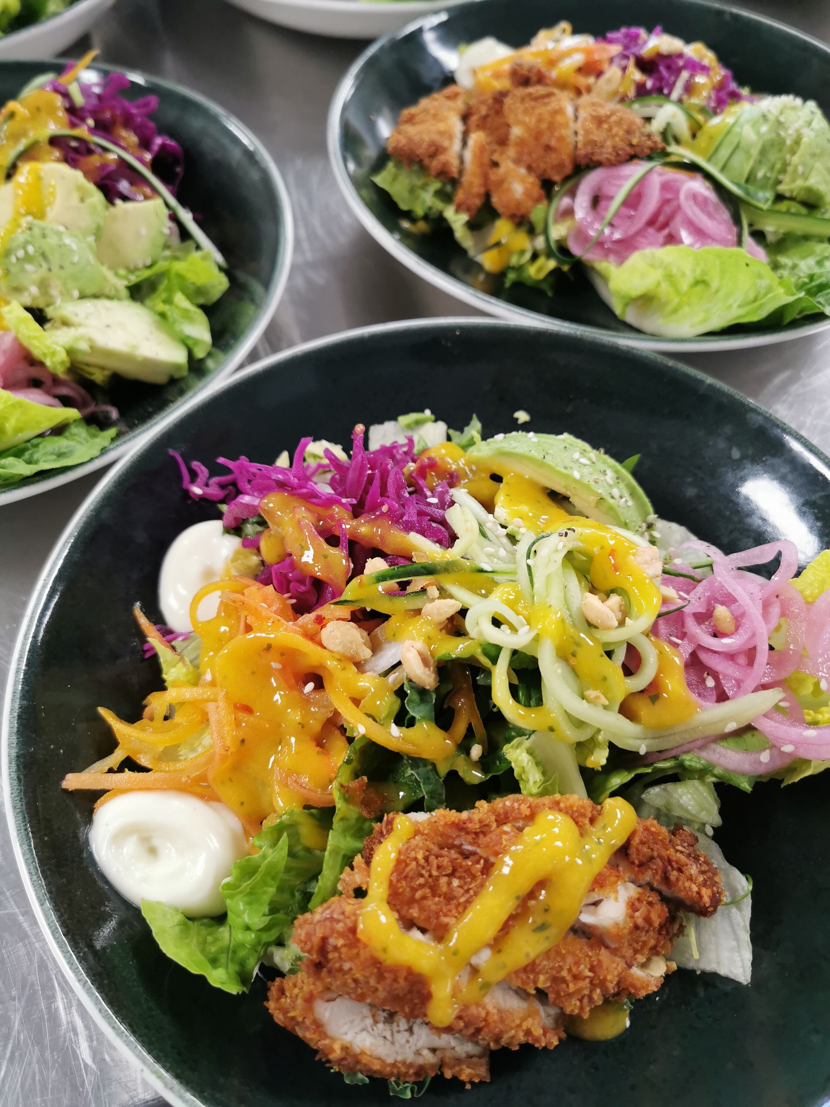 A variety of dishes including salads with shredded vegetables, a fried chicken breast, and a creamy sauce.