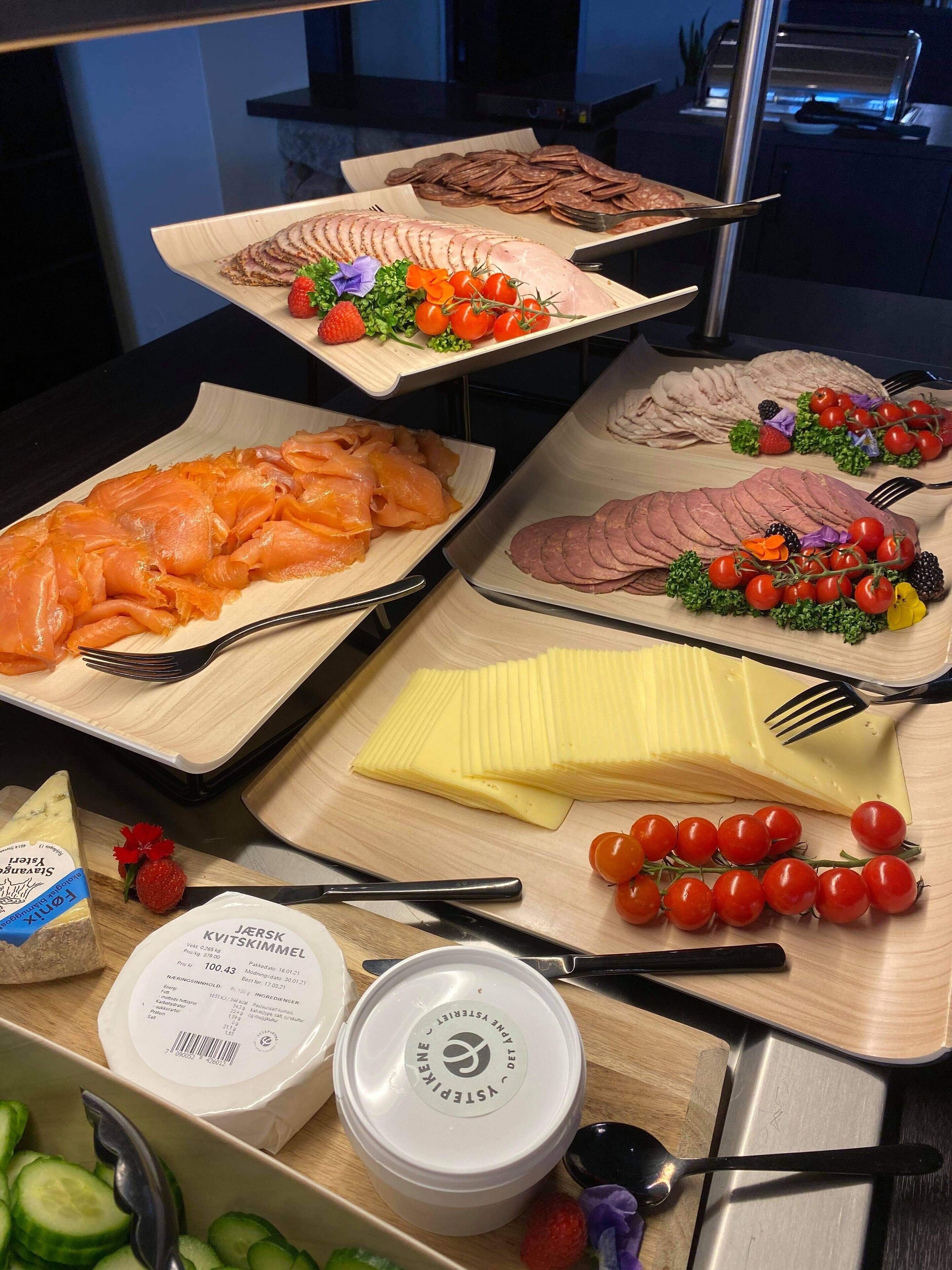 Un buffet proposant une variété de plats, notamment du saumon, du jambon, du fromage et des légumes frais.