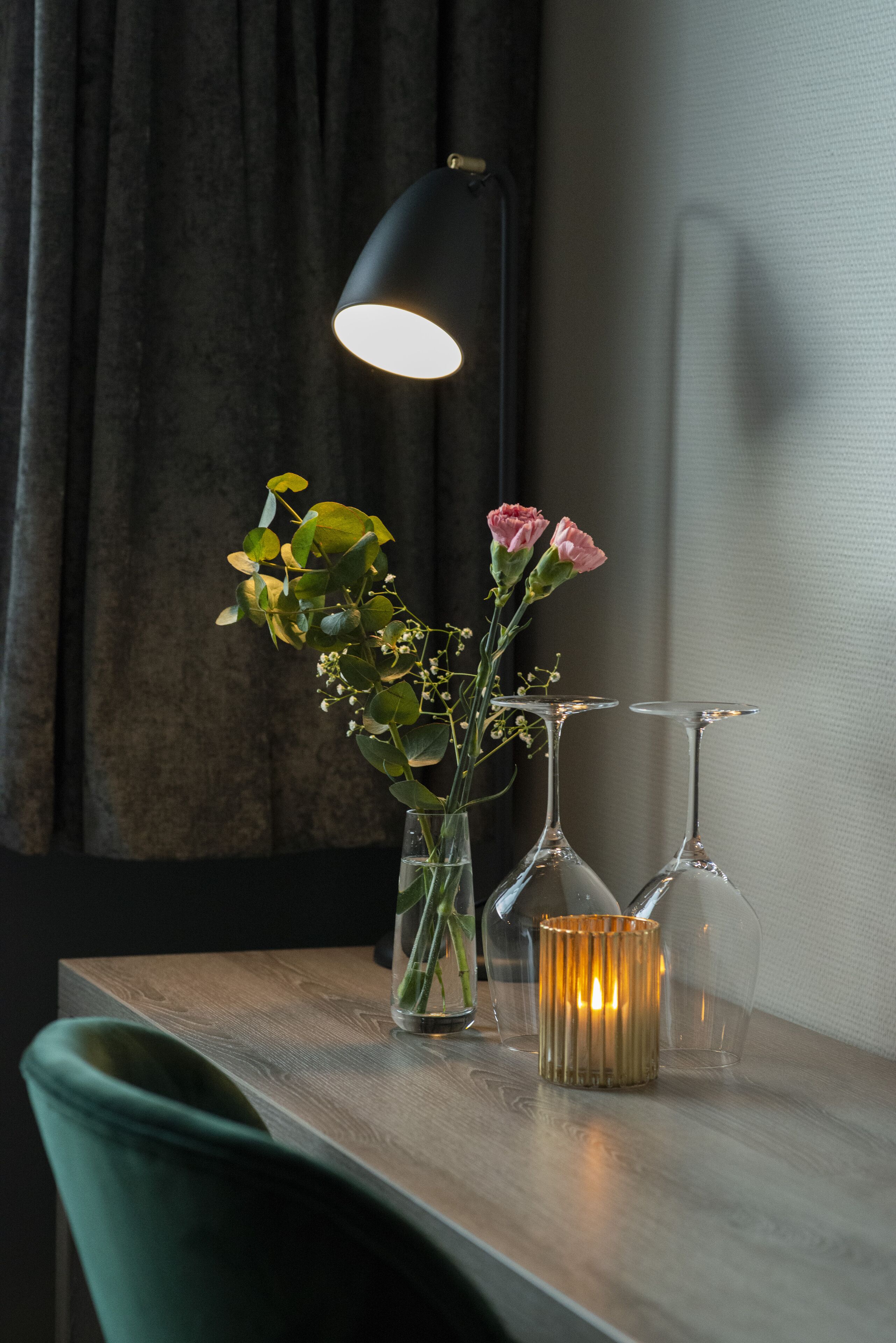 Una mesa de madera con un florero, dos copas de vino y una vela.