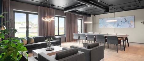 A modern office space with a large table, multiple chairs, sofas, and a large window with curtains.