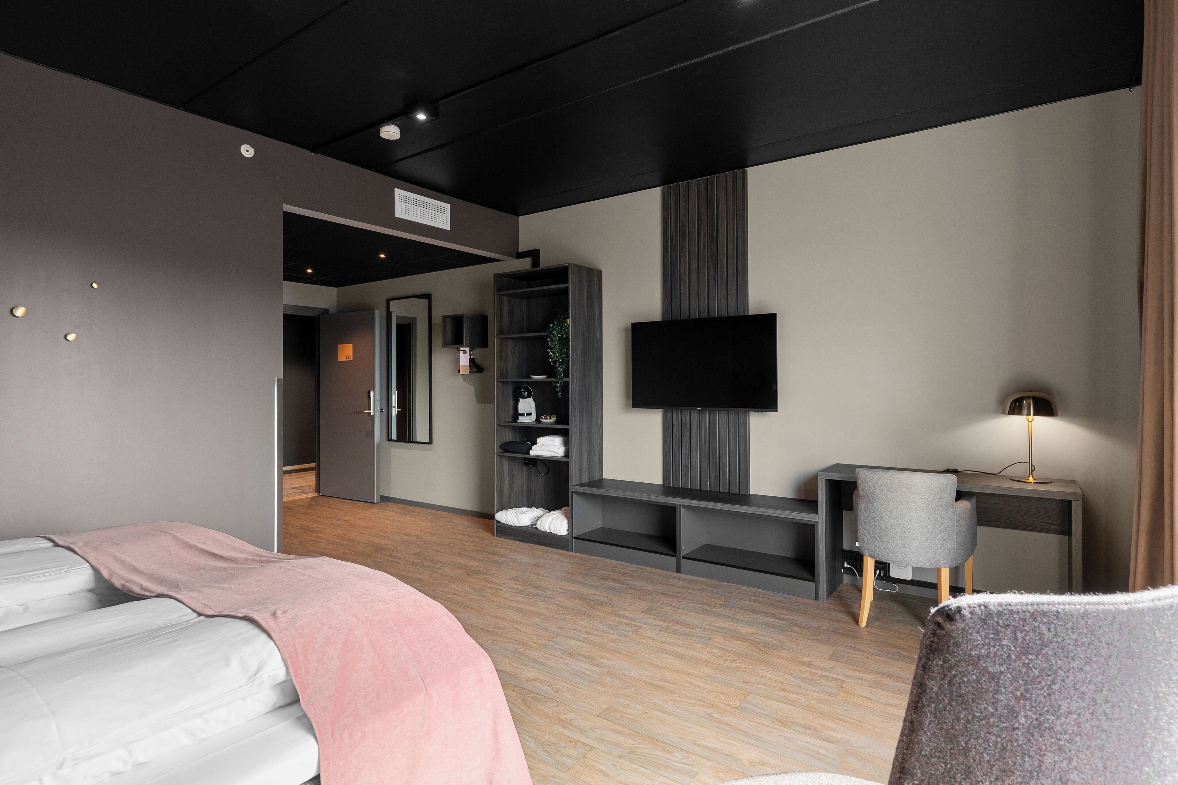 Una habitación de hotel moderna con cama, escritorio, televisión y armario.