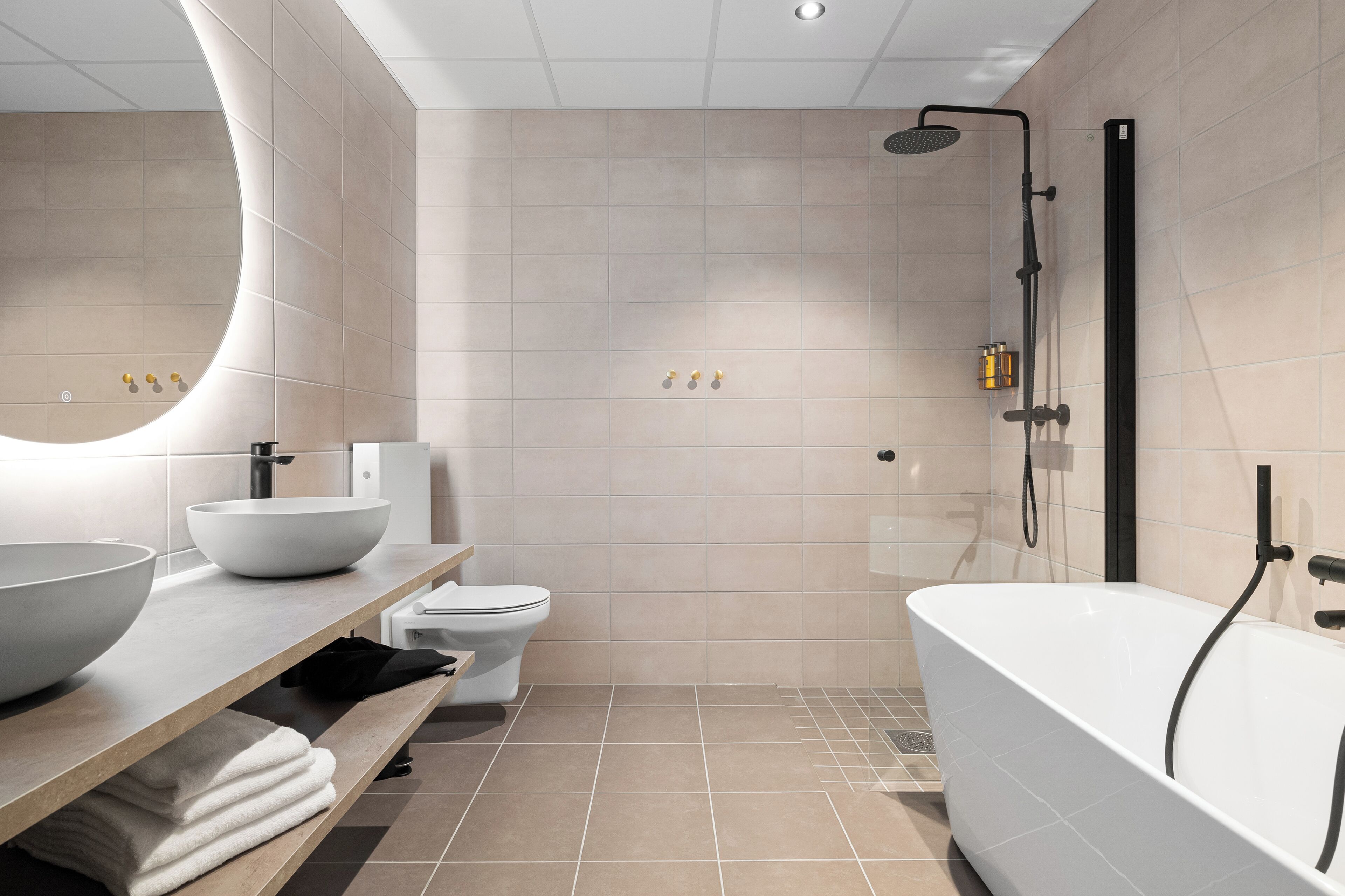 A modern bathroom with a freestanding bathtub, a large mirror, a white sink, and a toilet.