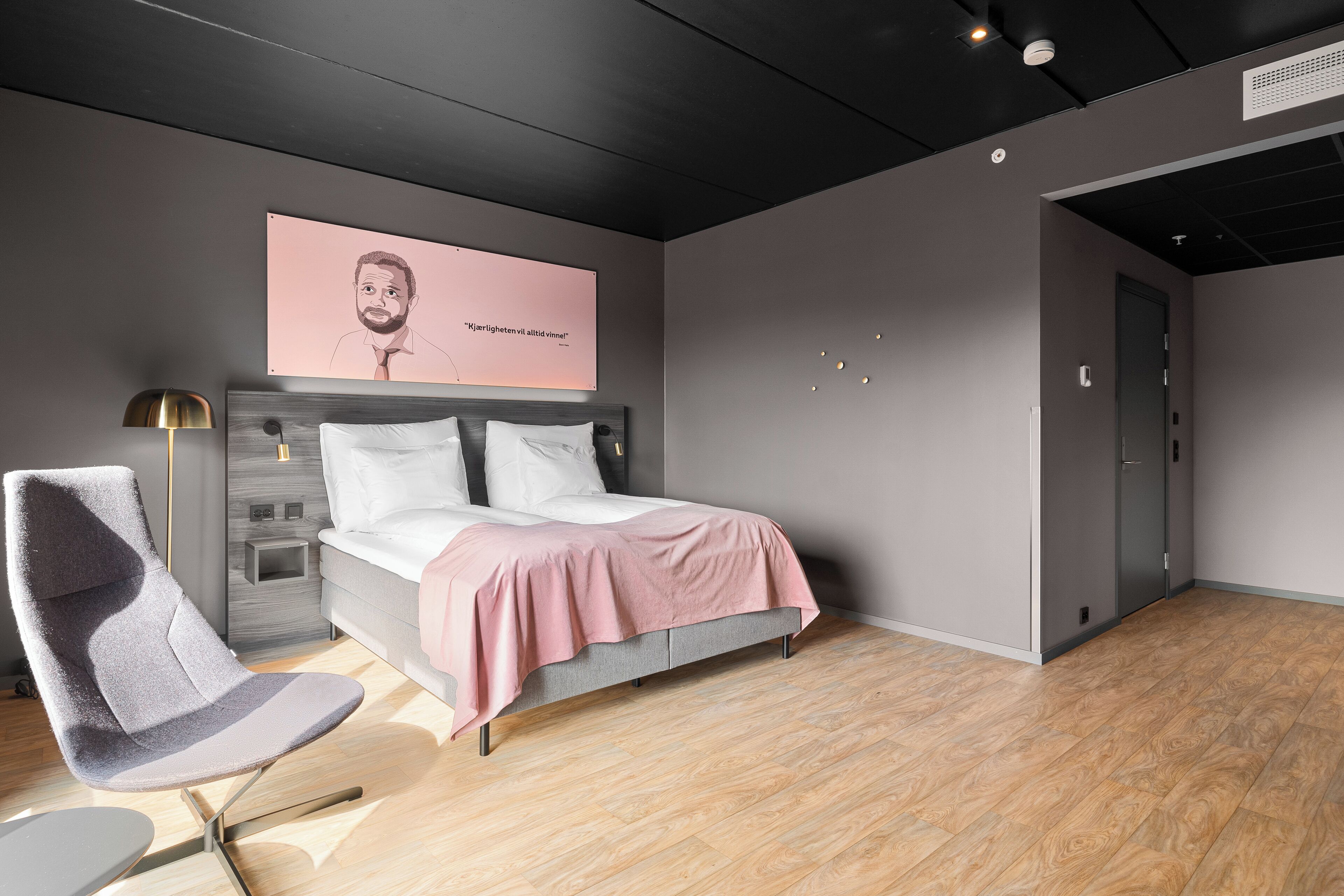 A modern bedroom with a bed, a chair, and a wall-mounted artwork.
