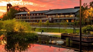A modern building with a clock tower, surrounded by a reflective pond and well-maintained gardens. - Hotell Jæren (Time)