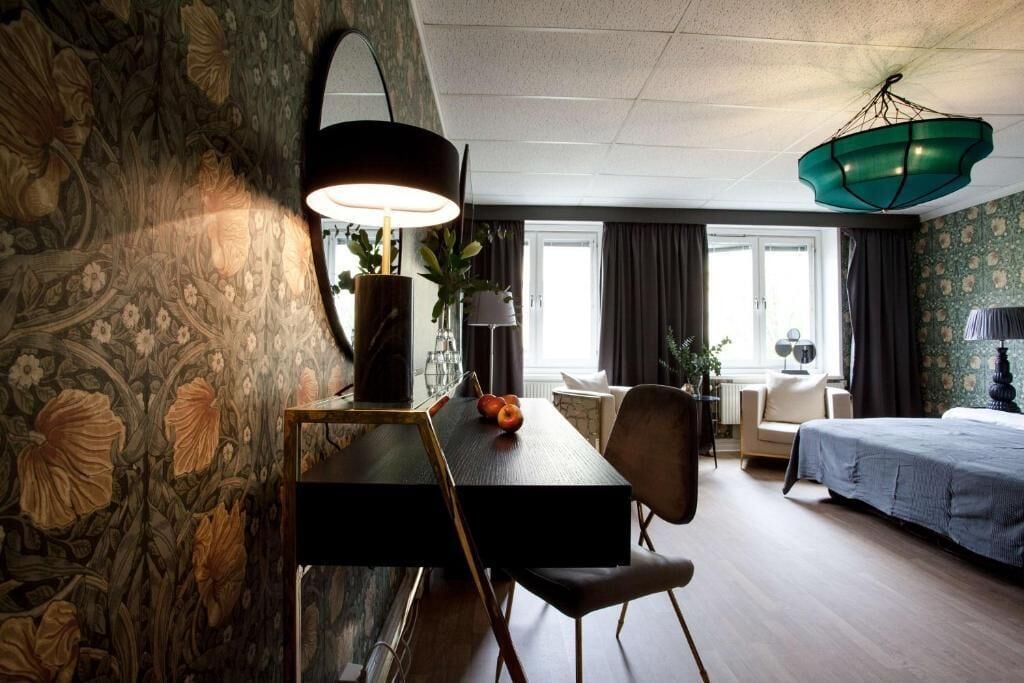 Habitación de hotel con mesa de comedor, sillas, cama y un amplio ventanal.