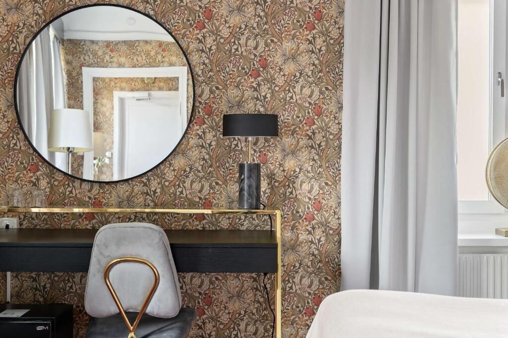 Une chambre d’hôtel avec un miroir rond, un bureau avec une lampe, une chaise et un lit.