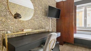A room with a dark wooden desk, a round mirror, a flat-screen TV, and a patterned wallpaper.