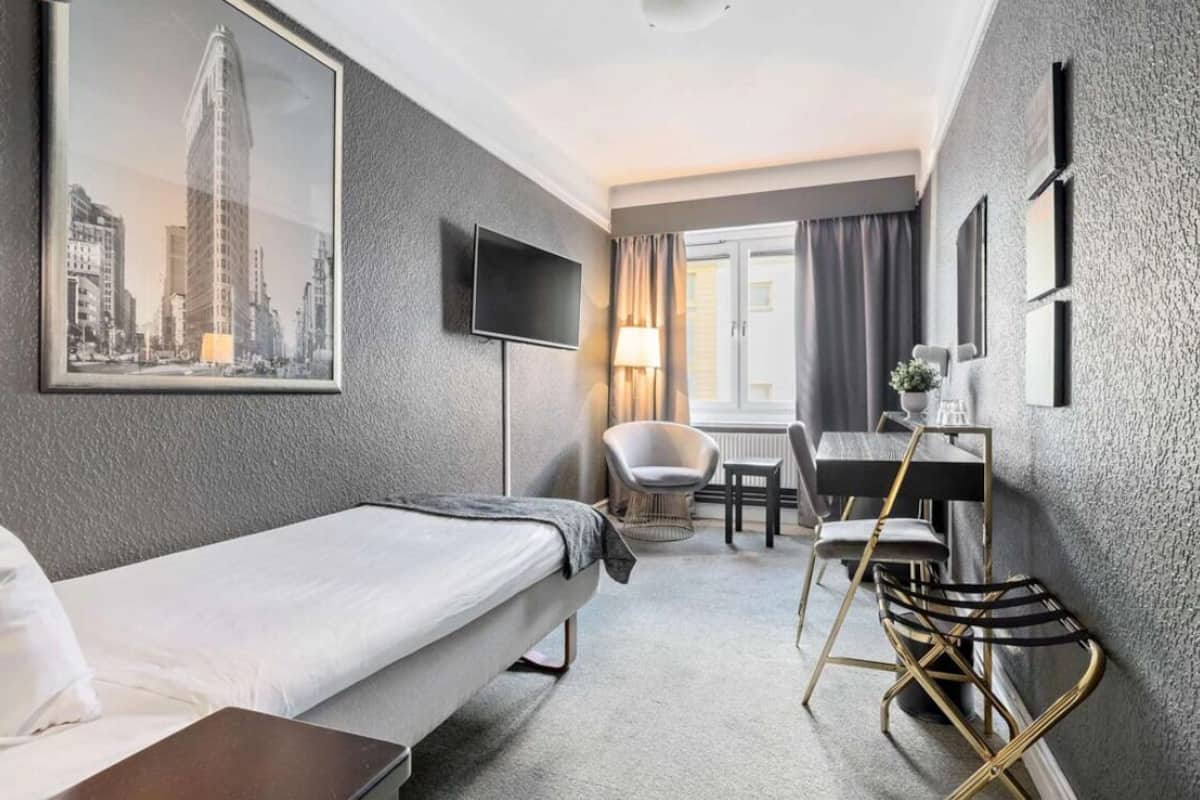Une chambre d’hôtel comprenant un lit, un bureau avec une chaise, une télévision et une fenêtre avec des rideaux.