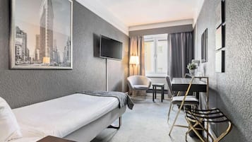 A hotel room with a bed, a desk with a chair, a television, and a window with curtains.