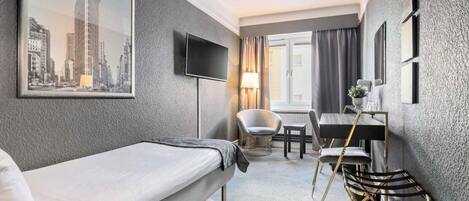 Habitación de hotel con cama, escritorio con silla, televisor y ventana con cortinas.