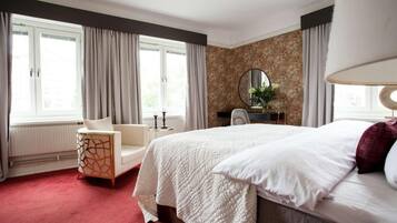 Ett hotellrum med en stor säng, en stol, en rund spegel och ett fönster med gardiner.