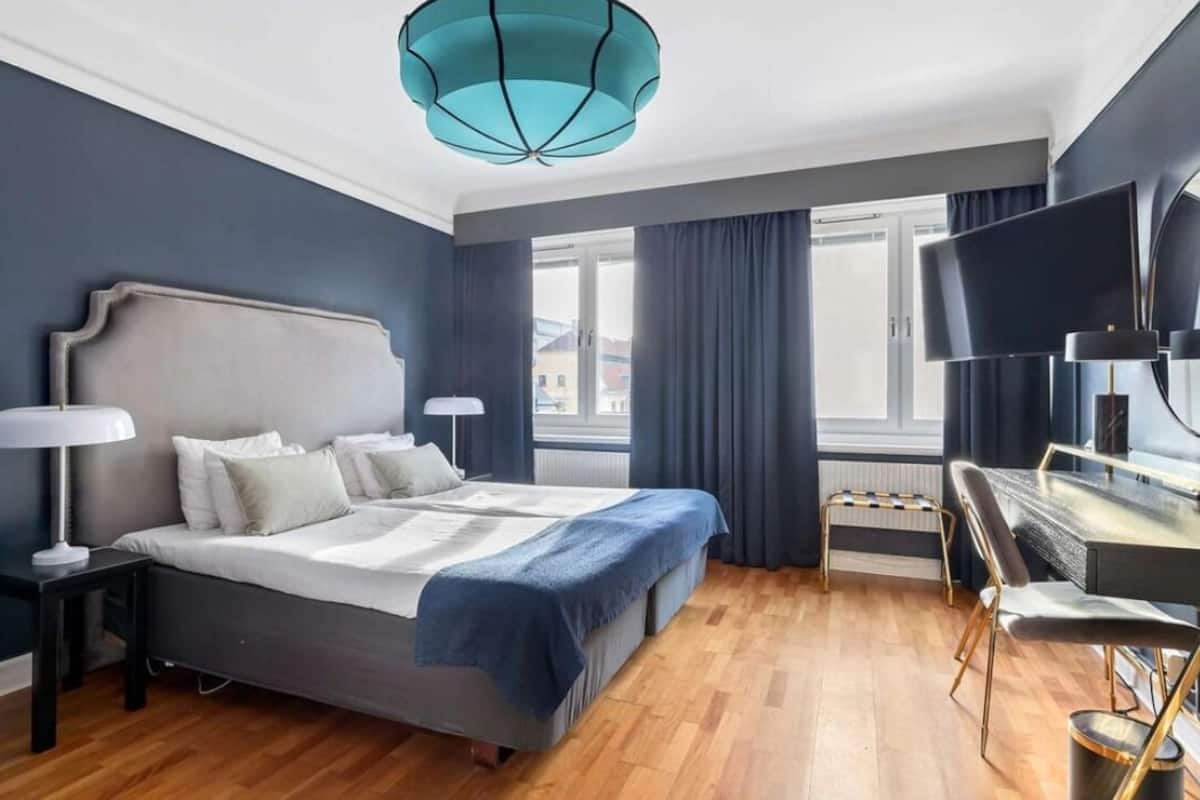 Une chambre d’hôtel moderne dotée d’un grand lit, d’un bureau avec une chaise, d’une télévision et d’une fenêtre avec des rideaux.