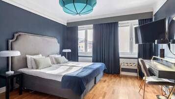 Una habitación de hotel moderna con una cama grande, un escritorio con silla, un televisor y una ventana con cortinas.