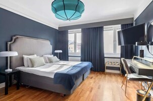 Una habitación de hotel moderna con una cama grande, un escritorio con silla, un televisor y una ventana con cortinas.