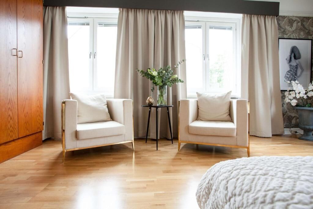 Et soveværelse med to lænestole, et lille bord med en vase og en stor seng.