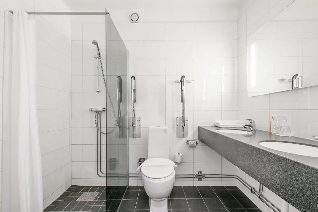 A modern bathroom with a glass-enclosed shower, a white toilet, and a granite countertop with a sink and mirror.