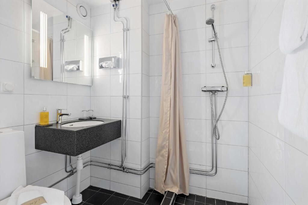 A bathroom with a sink, mirror, shower, and towel rack.