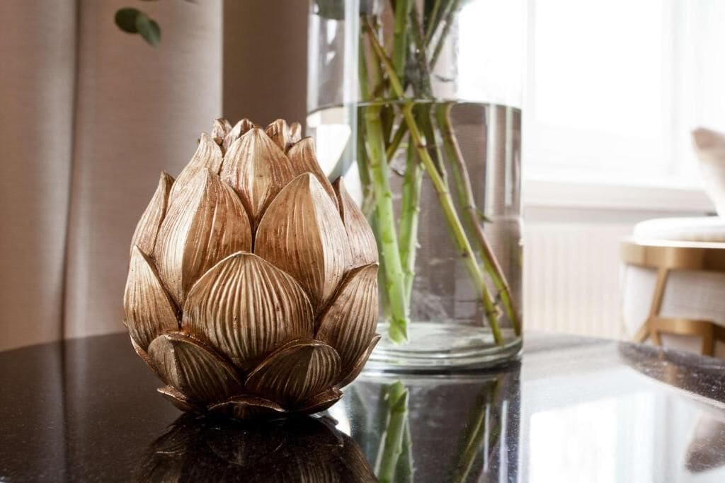 A lotus flower sculpture on a reflective surface with a glass vase containing green plants in the background.