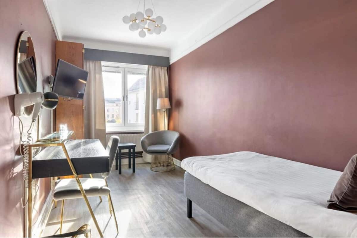 Une chambre d’hôtel avec un lit, un bureau équipé d’un ordinateur, une chaise, une lampe et une grande fenêtre.