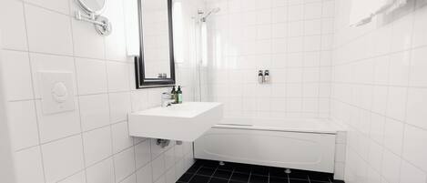 Un baño con lavamanos, espejo e inodoro blancos, suelo de baldosas negras y bañera blanca.