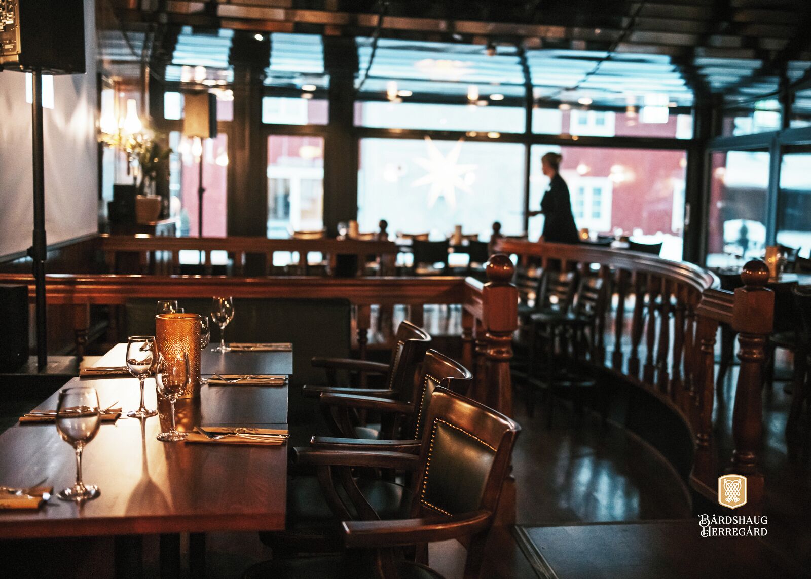 Un comedor interior con mesas y sillas de madera, una barra y amplias ventanas que dejan entrar luz natural.