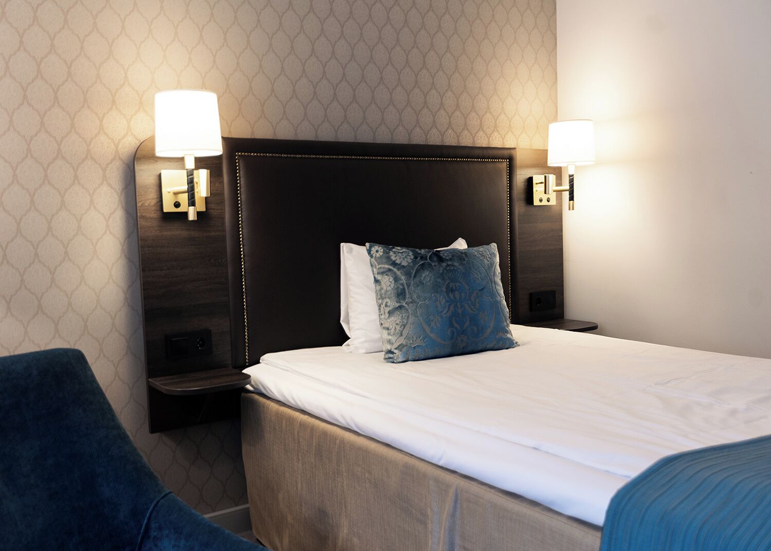 A hotel room with a large bed, two bedside lamps, and a blue chair.