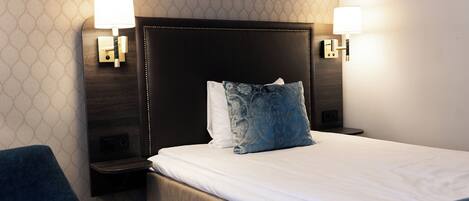 A hotel room with a large bed, two bedside lamps, and a blue chair.