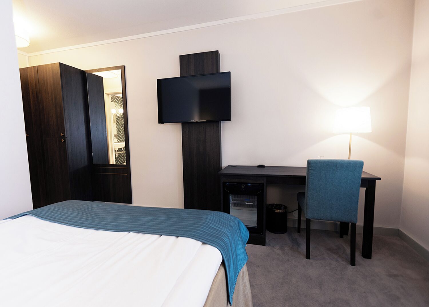Een hotelkamer met een bed, een bureau, een stoel, een televisie en een lamp.
