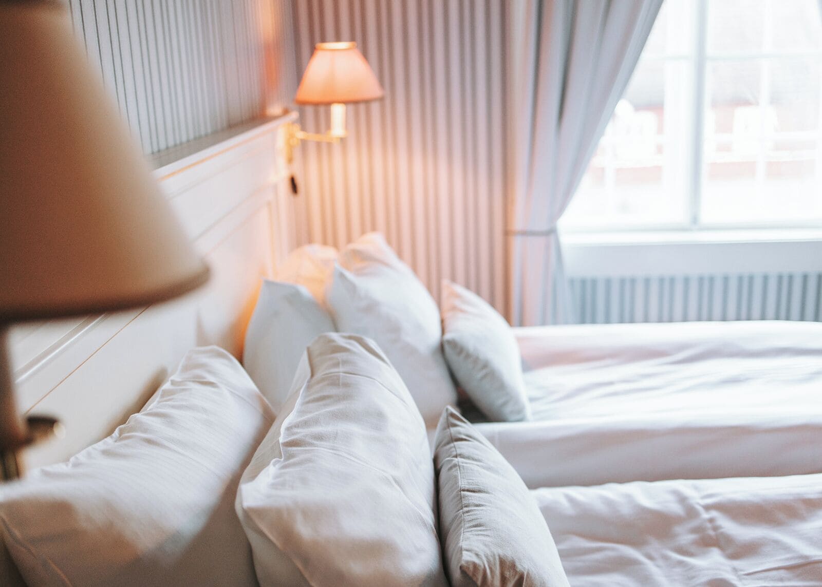 Ein Hotelzimmer mit Bett, Kissen, einer Lampe und einem Fenster mit Vorhängen.