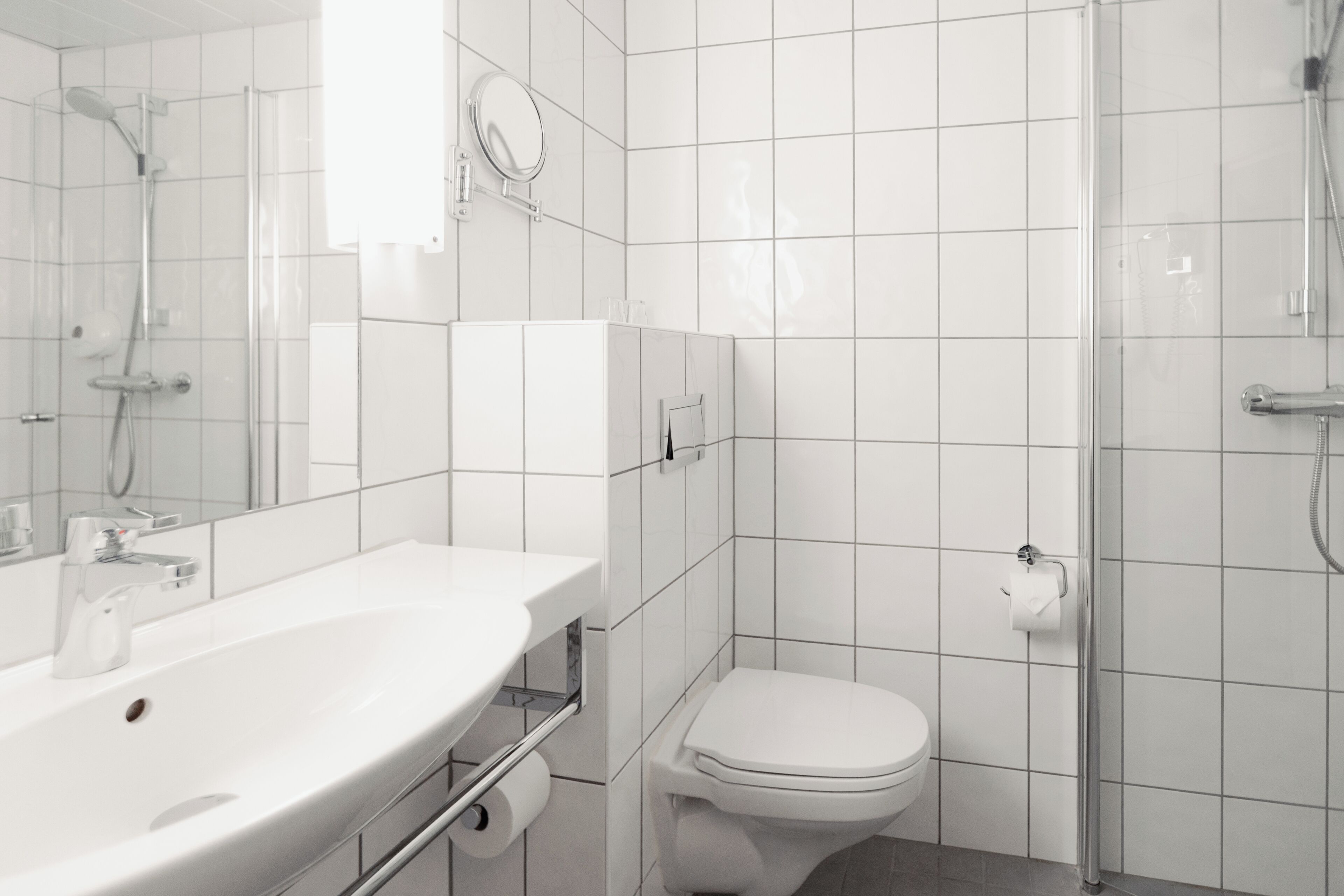 Un baño moderno con lavamanos, inodoro y ducha blancos.