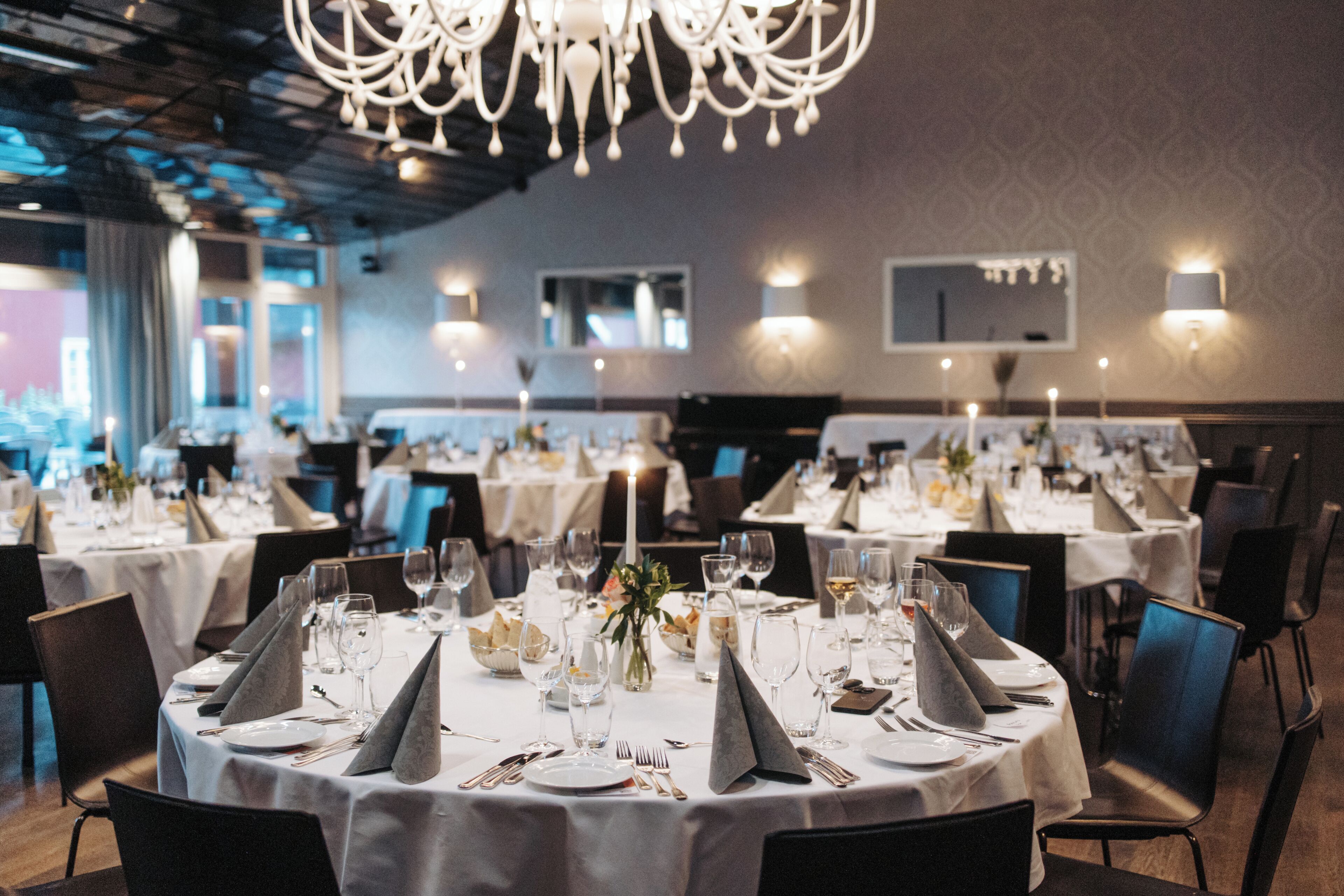 A restaurant with round tables set for dining, featuring white tablecloths, silverware, and glassware.
