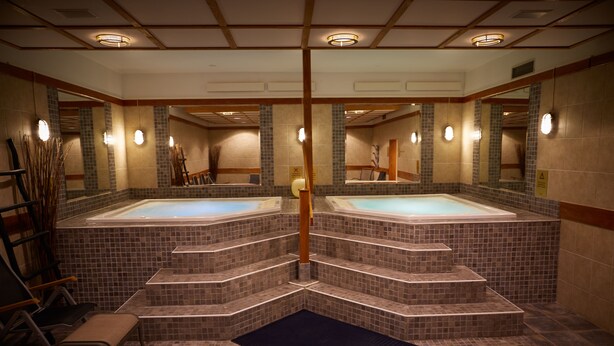 A spa area with two hot tubs, tiled walls, and a wooden bench.