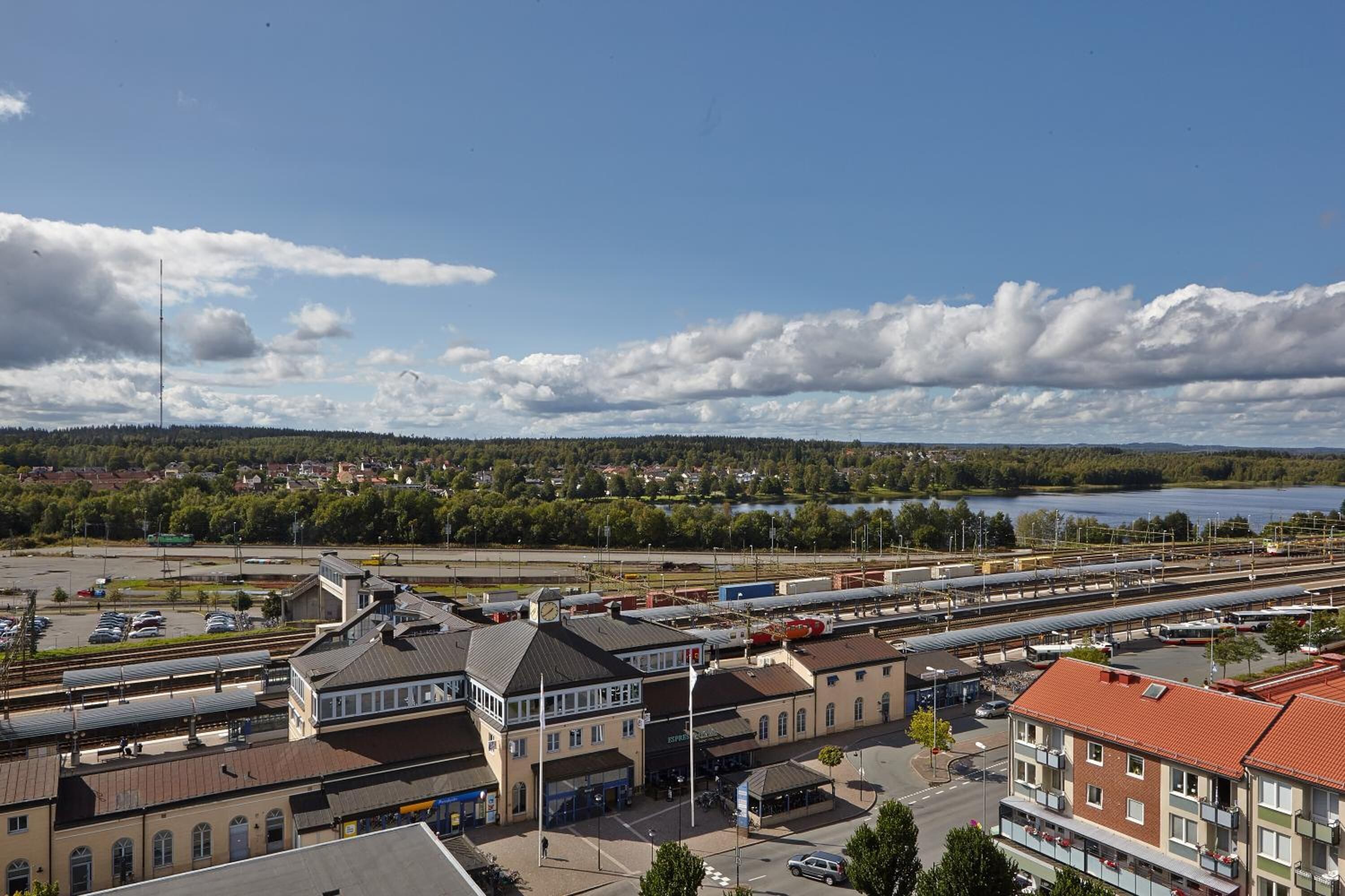 A train station with multiple tracks, a clock tower, and a lake in the background.