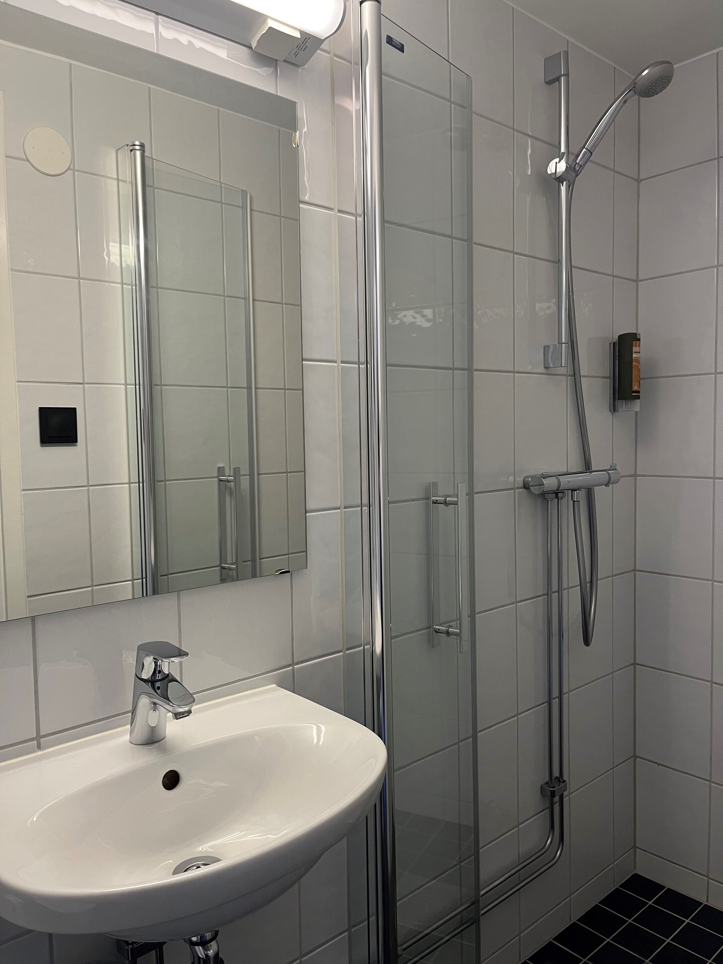 Ein modernes Badezimmer mit einem weißen Waschbecken, einer Duschkabine aus Glas und einem Spiegel.