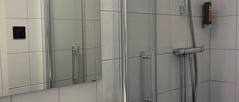 Ein modernes Badezimmer mit einem weißen Waschbecken, einer Duschkabine aus Glas und einem Spiegel.