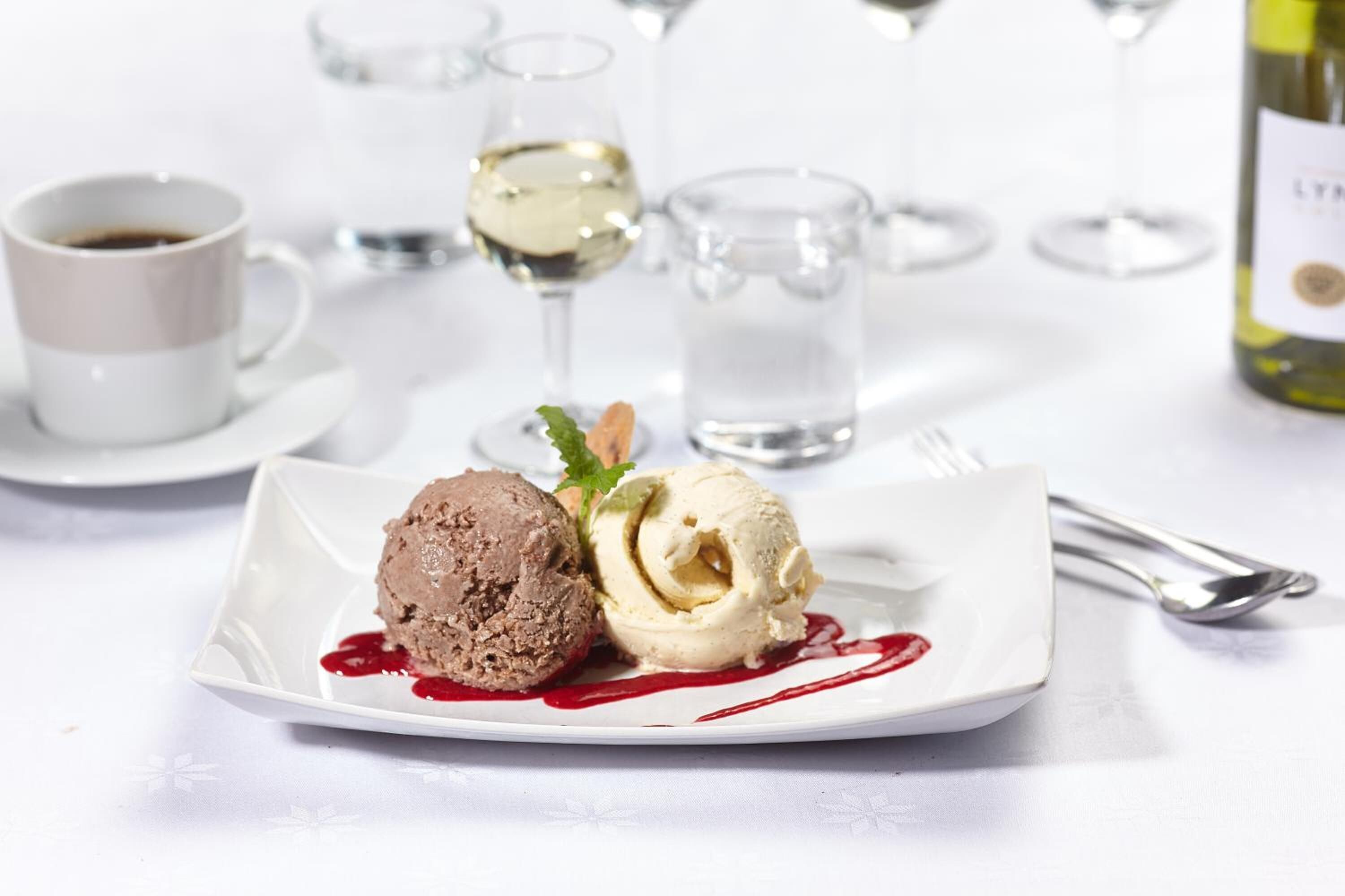En desserttallerken med to kugler is, et glas hvidvin og en vinflaske på et hvidt bord.
