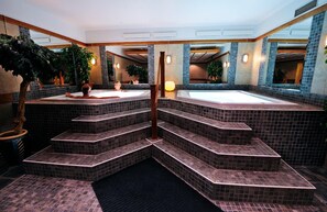 Uma área de spa com uma banheira de hidromassagem central, vários degraus que a levam e diversas plantas em vasos.