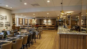 A modern hotel lobby with a central bar area, multiple seating arrangements, and a wooden reception desk.