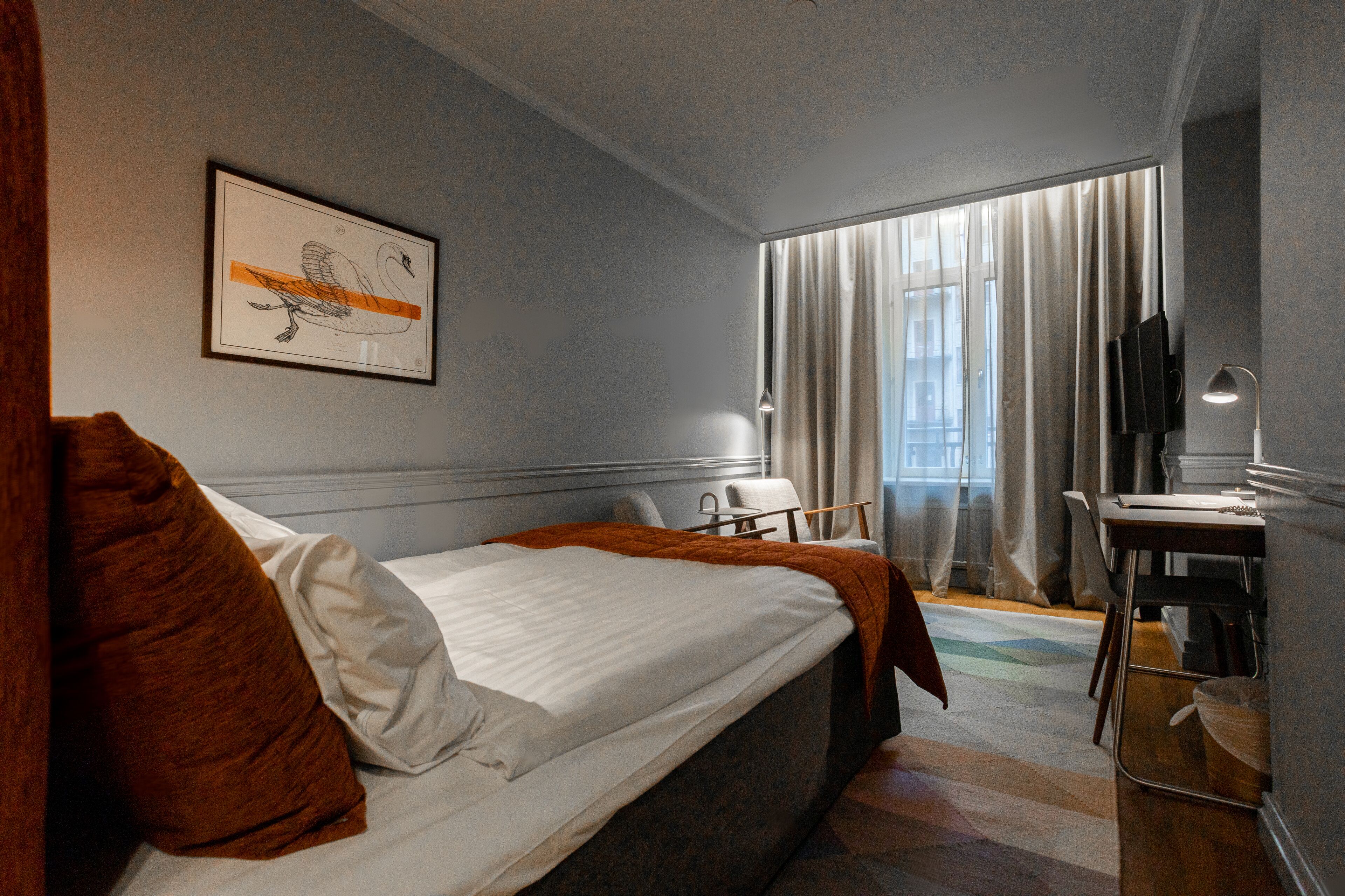 A hotel room with a bed, a desk, a chair, a TV, and a window with curtains.