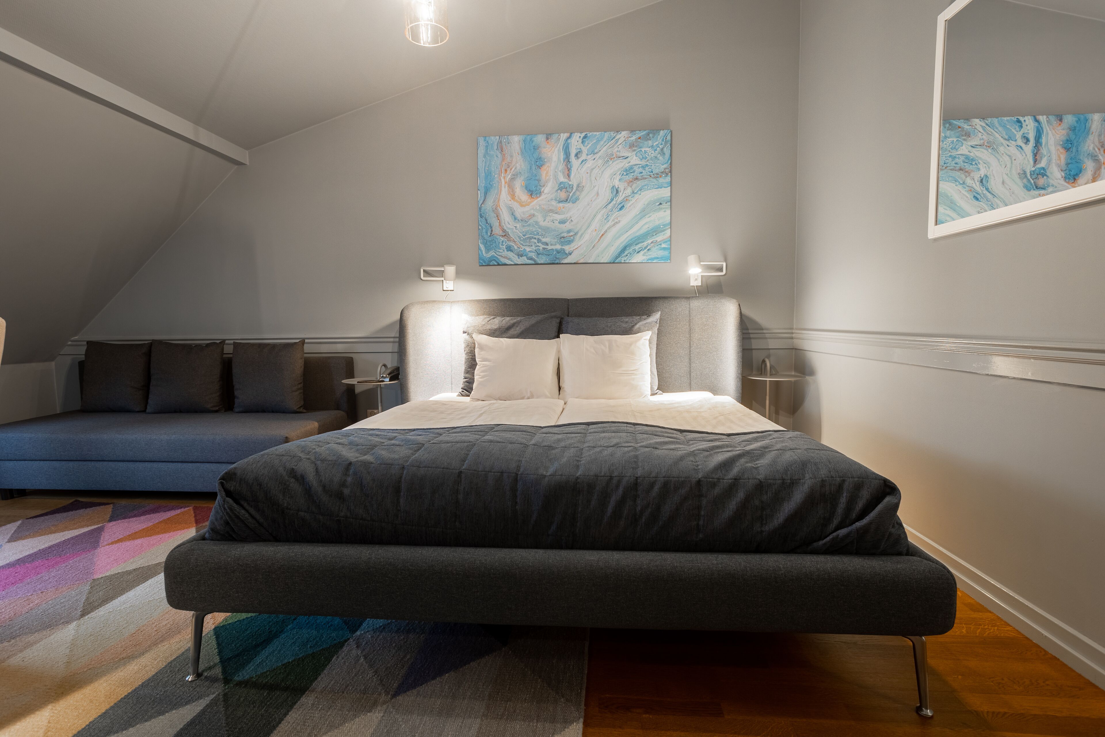 Un dormitorio moderno con cama, sofá y un cuadro abstracto grande en la pared.