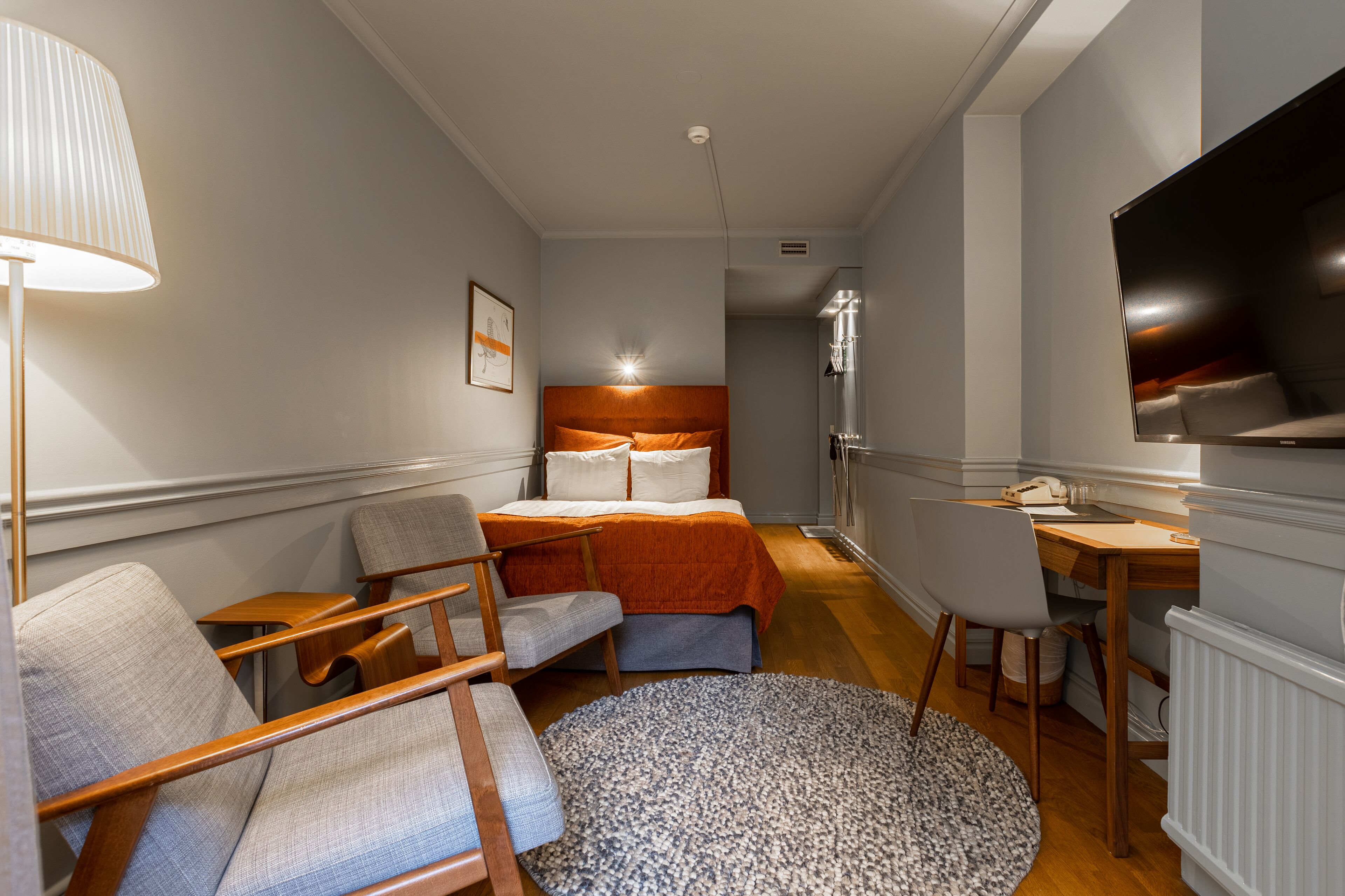 Habitación de hotel con cama, escritorio, silla, lámpara y televisión.