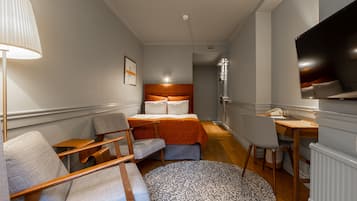 Habitación de hotel con cama, escritorio, silla, lámpara y televisión.