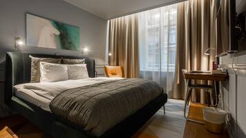 A modern hotel room with a large bed, a desk, a chair, and a window with curtains.