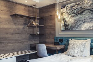 A modern hotel room with a wooden wall, a bed with a blue headboard, a desk with a chair, and a wall-mounted clock. - Hotel Poseidon (Gothenburg)