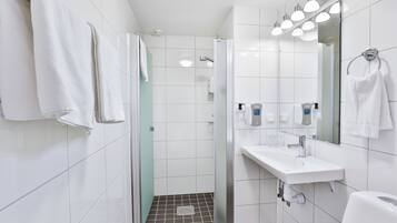 A modern bathroom with white tiles, a glass shower enclosure, a white sink with a mirror, and a towel rack.