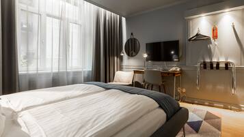 A hotel room with a large bed, a desk, a chair, a TV, and a wardrobe with a mirror.