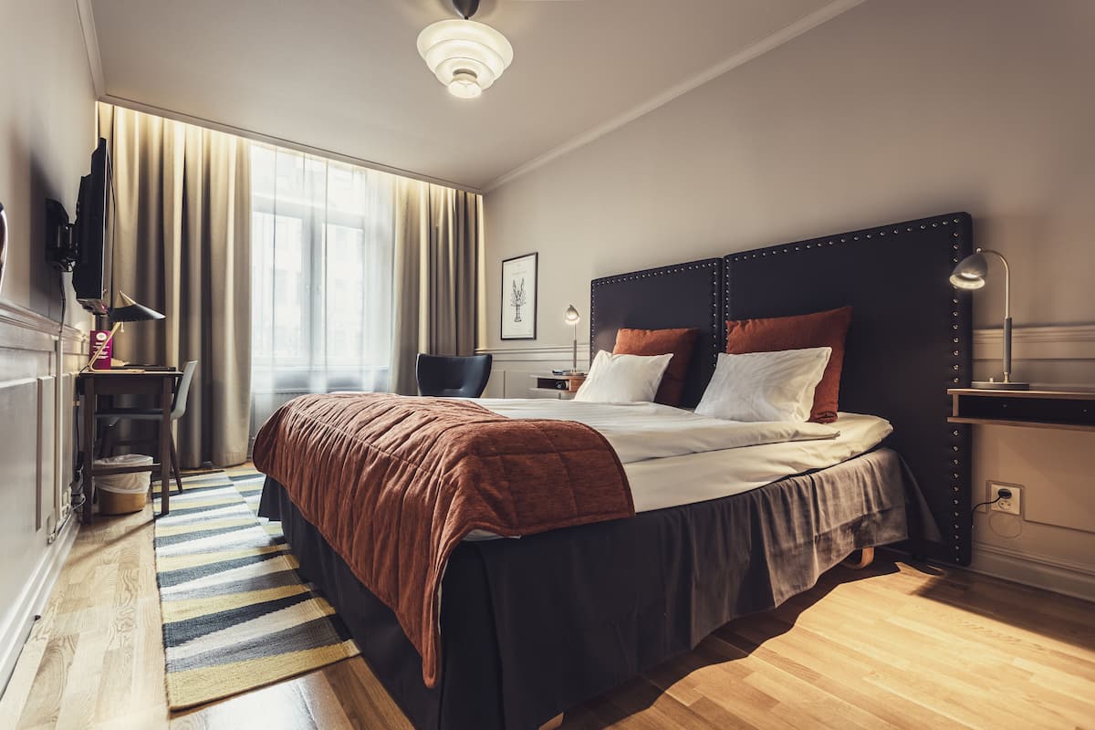 A modern hotel room with a large bed, a desk, a chair, and a television.