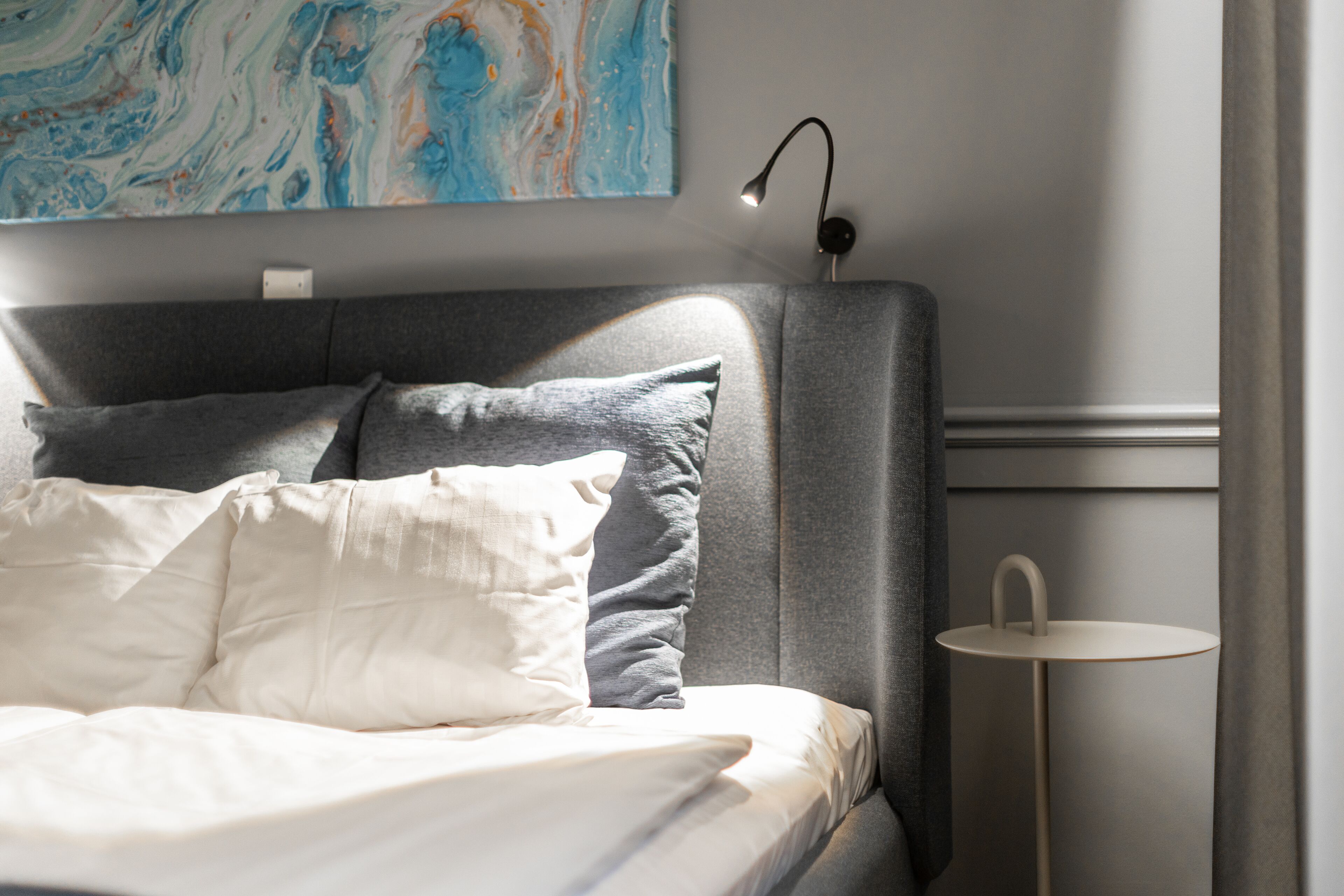 Un lit bien fait, avec des oreillers, une lampe de chevet et une petite table ronde placée à côté.