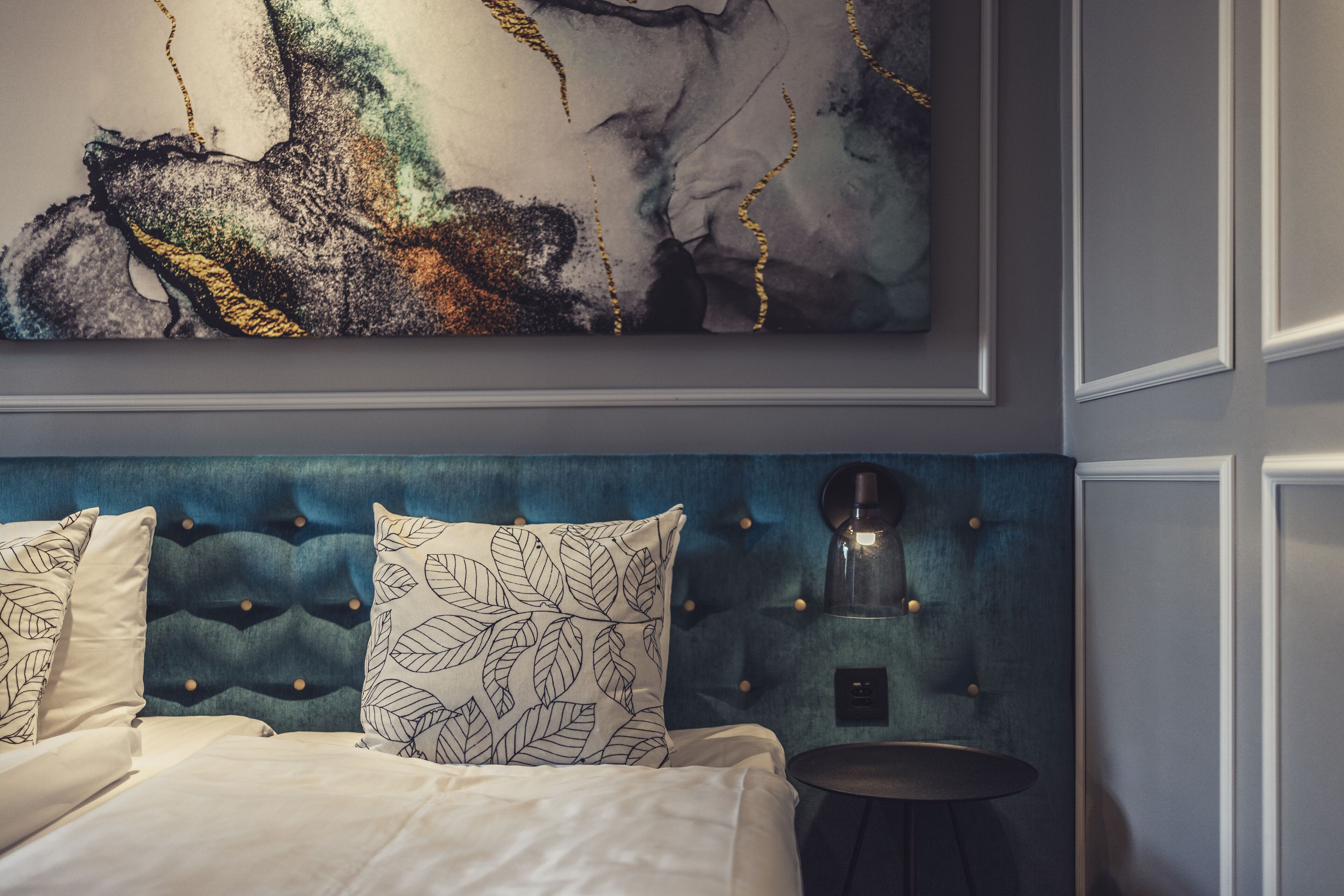 Een slaapkamer met een gestuwd hoofdeinde, een bed met witte lakens en een wandgemonteerde koffiezetapparaat.